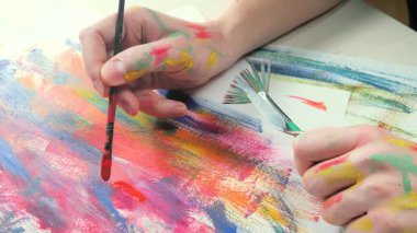 Sanatçının elleri, sanatta yaratıcı imgeler yaratmak için çalışır. Resim boyaları ve fırçalar, palet, guaj ve suluboya kullanarak tuvale çok renkli dokunuşlar uyguluyorlar..