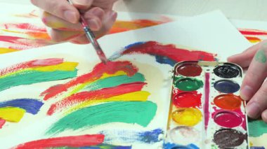 Sanatçının elleri, sanatta yaratıcı imgeler yaratmak için çalışır. Resim boyaları ve fırçalar, palet, guaj ve suluboya kullanarak tuvale çok renkli dokunuşlar uyguluyorlar..