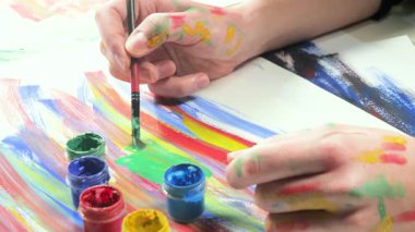 Sanatçının elleri, sanatta yaratıcı imgeler yaratmak için çalışır. Resim boyaları ve fırçalar, palet, guaj ve suluboya kullanarak tuvale çok renkli dokunuşlar uyguluyorlar..