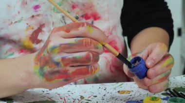 Sanatçının elleri, sanatta yaratıcı imgeler yaratmak için çalışır. Resim boyaları ve fırçalar, palet, guaj ve suluboya kullanarak tuvale çok renkli dokunuşlar uyguluyorlar..