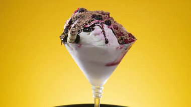 Çikolatalı şekerle kaplı cam bir kadehte meyveli dondurma yavaşça kendi ekseni etrafında döner.