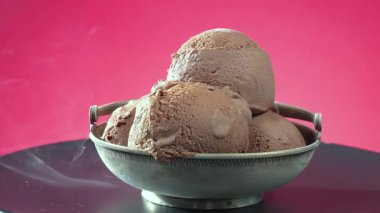 Metal bardakta çikolatalı dondurma, parlak bir arka planda yavaşça dönüyor.,