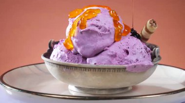 Cam bir kasede meyveli dondurma, parlak bir arka planda yavaşça dönüyor, üzerine çikolata parçacıkları serpiştirilmiş..