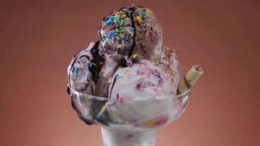 Cam bir kasede çikolatalı dondurma, parlak bir arka planda yavaşça dönüyor.