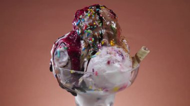 Metal bir kasede çikolatalı dondurma, yenilebilir konfeti serpiştirilir, parlak bir arka plana doğru yavaşça döner, sıcaklığın etkisiyle erir..
