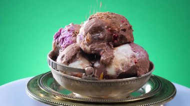 Metal bir kasede çikolatalı dondurma, yenilebilir konfeti serpiştirilmiş, parlak bir arka planda yavaşça dönüyor..