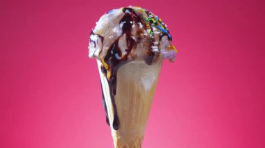 Waffle külahındaki dondurma, parlak bir arkaplan karşısında yavaşça kendi ekseni etrafında döner ve ısı etkisiyle erir..