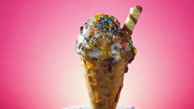 Waffle külahındaki dondurma, parlak bir arkaplan karşısında yavaşça kendi ekseni etrafında döner ve ısı etkisiyle erir..
