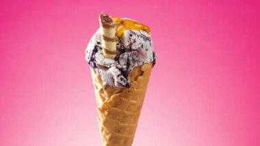 Waffle külahındaki dondurma, parlak bir zemin üzerinde yavaşça kendi ekseni etrafında döner, meyve şurubu yavaşça üzerine dökülür.