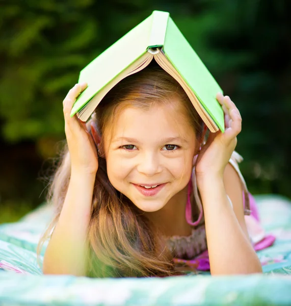 Menina está se escondendo sob livro ao ar livre — Fotografia de Stock