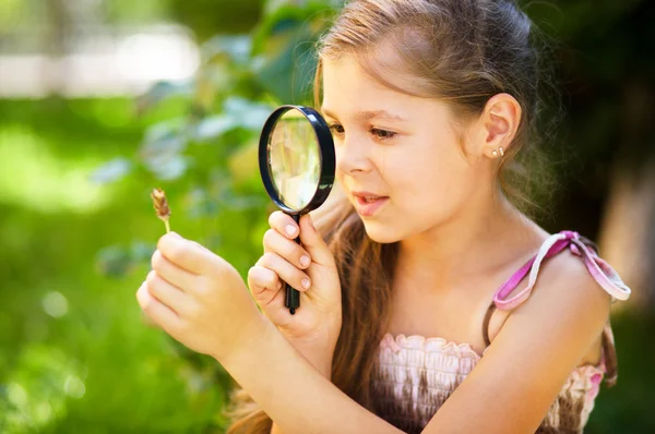 Young girl is looking at flower through magnifier — Stock Photo, Image