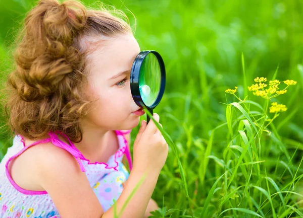 Young girl is looking at flower through magnifier — Stock Photo, Image
