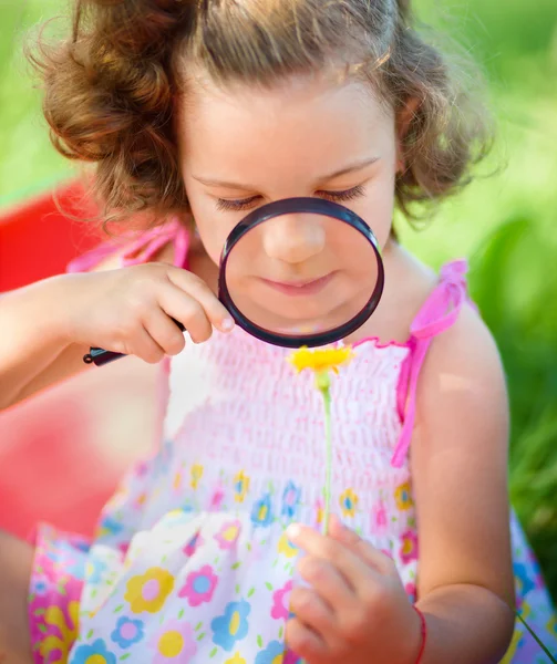 Young girl is looking at flower through magnifier — Stock Photo, Image