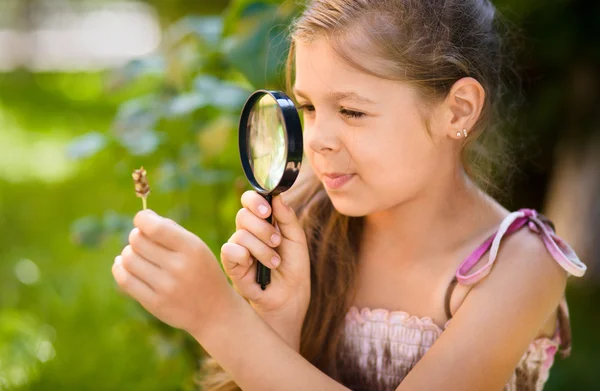 Young girl is looking at flower through magnifier — Stock Photo, Image