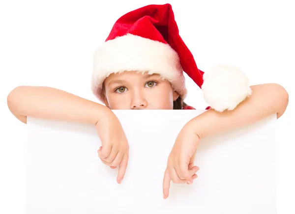 Kleines Mädchen mit Weihnachtsmütze hält leeres Brett — Stockfoto