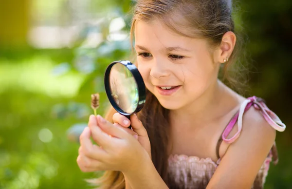 Young girl is looking at flower through magnifier — Stock Photo, Image