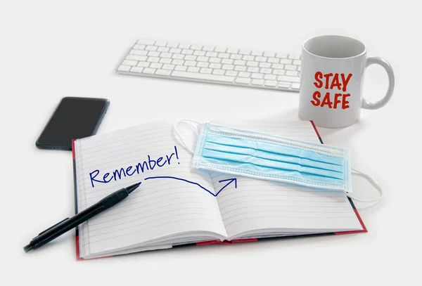 Remember to wear a protection mask at work during the Coronavirus  Covid-19 pandemic concept. Medical protection mask waiting at the desk along with note pad, computer keyboard, phone, pencil and a coffee mug.