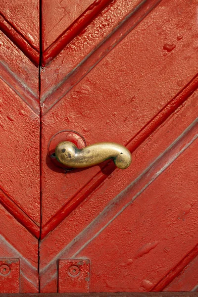 Close up of old brass door handle on a weathered red wooden door with profiles.