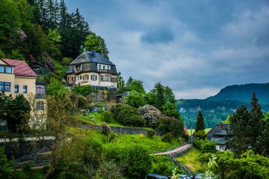 18 Mayıs 2019 Rathen, Saksonya, Almanya - Bastei Köprüsü 'nün karşısındaki Elbe nehri kıyısındaki küçük bir kasaba olan Kurort Rathen' da dar dağ yolları ve konut evleri