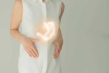 Beyaz elbiseli tanınmayan bir kadın hasta, ellerinde çizilmiş midesi var. İnsan sindirim sistemi kavramı.