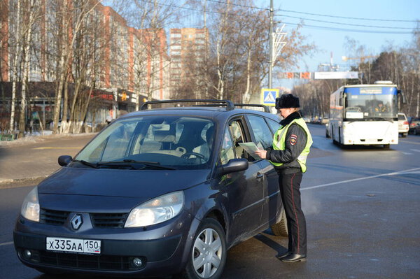 ОДИНЦОВО, МОСКОВСКАЯ ОБЛАСТЬ, РОССИЯ - 20 февраля 2016 года: Инспектор дорожно-патрульной службы полиции проверяет документы водителя остановленного автомобиля