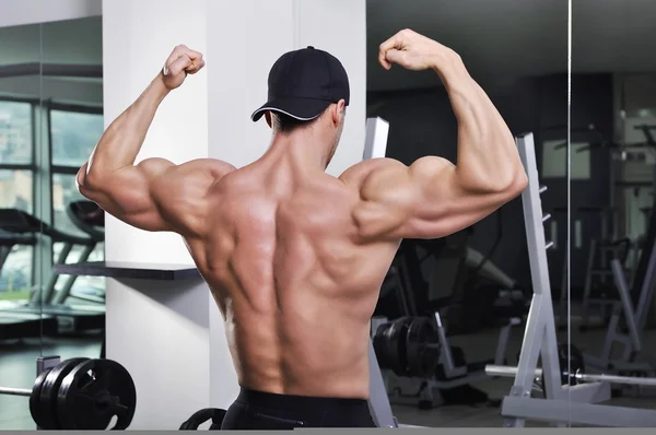 Vacker kraftfull atletisk man poserar på gymmet. Stark kroppsbyggare med perfekt muskulösa rygg, axlar och biceps. — Stockfoto