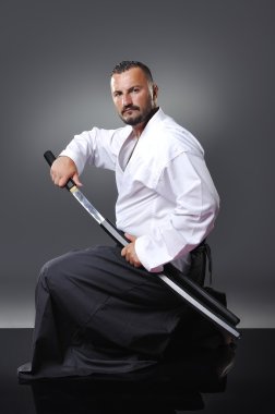 Yakışıklı genç siyah kuşak erkek karate gri arka plan üzerinde kılıç ile poz