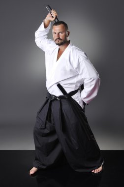 Yakışıklı genç siyah kuşak erkek karate gri arka plan üzerinde kılıç ile poz