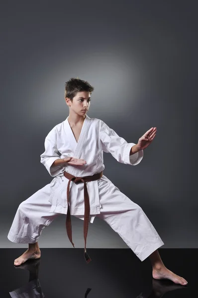 Hermoso joven karate masculino haciendo kata sobre el fondo gris — Foto de Stock