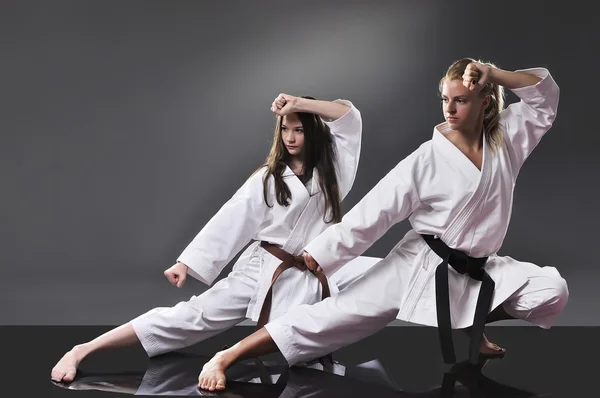 Dos hermosas jóvenes karate hembra haciendo kata sobre el fondo gris — Foto de Stock
