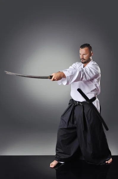 Bonito jovem cinturão preto karatê masculino posando com espada no fundo cinza — Fotografia de Stock