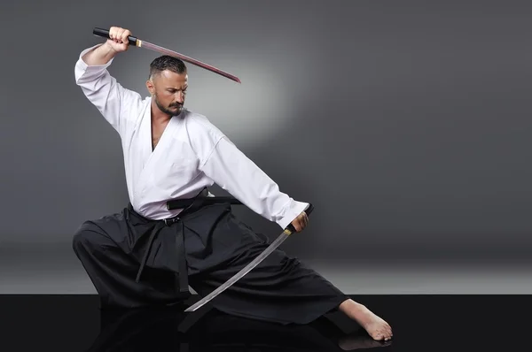 Stilig ung svart bälte manliga karate poserar med svärd på den grå bakgrunden — Stockfoto