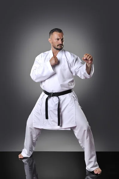 Przystojny młody mężczyzna karate robi kata na szarym tle — Zdjęcie stockowe