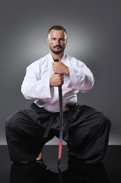 Pohledný mladý černý pás mužské karate pózuje s mečem na šedém pozadí — Stock fotografie