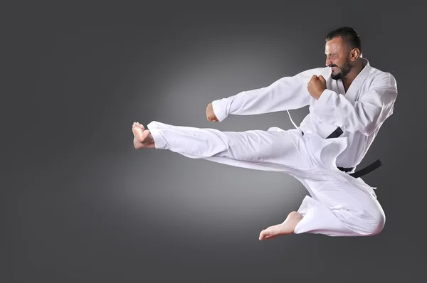 Przystojny młody czarny pas karate mężczyzna, robi kick na szarym tle — Zdjęcie stockowe
