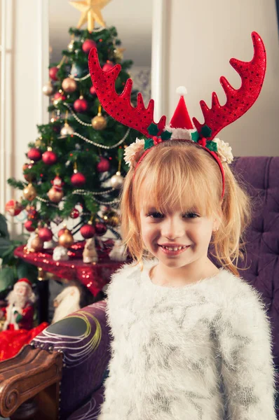 Gyönyörű Kislány Szarvakkal Karácsonyfa Mellett Áll Mosolyog — Stock Fotó