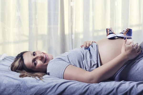 Små skor för det ofödda barnet på magen på gravid kvinna — Stockfoto