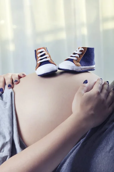 Små skor för det ofödda barnet på magen på gravid kvinna — Stockfoto