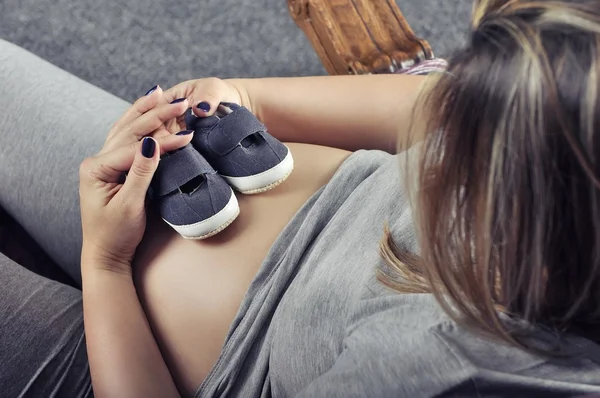 Маленькая обувь для будущего ребенка на животе беременной женщины — стоковое фото