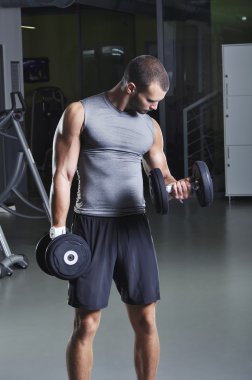 Pazı egzersiz yaparak Dumbbells ile ayakta pozisyonda yakışıklı kaslı erkek modeli