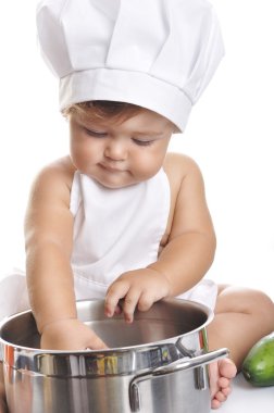 Funny adorable baby boy chef sitting and playing with kitchen equipment