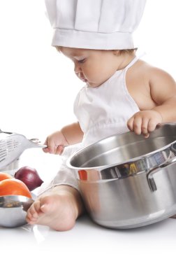 Funny adorable baby boy chef sitting and playing with kitchen equipment