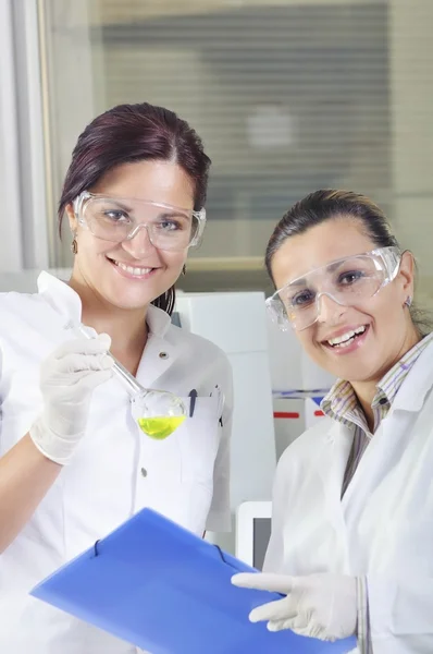 Attractive young PhD students scientists observing the green indicator color shift after the solution destillation in chemical laboratory — Stock Photo, Image