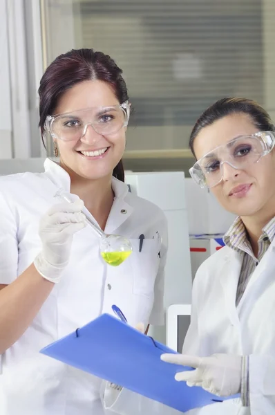 Attractive young PhD students scientists observing the green indicator color shift after the solution destillation in chemical laboratory — 图库照片