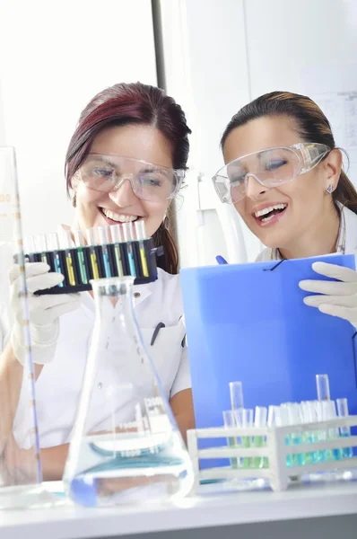 Jovens cientistas estudantes de doutorado atraentes observando a mudança de cor indicador azul, amarelo e verde após a destilação da solução em laboratório químico — Fotografia de Stock