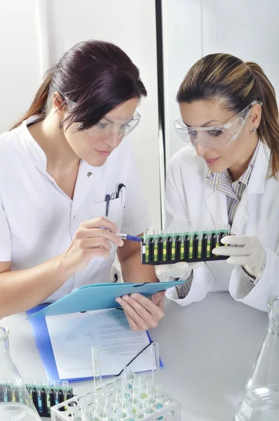 Jovens cientistas estudantes de doutorado atraentes observando a mudança de cor indicador azul, amarelo e verde após a destilação da solução em laboratório químico — Fotografia de Stock