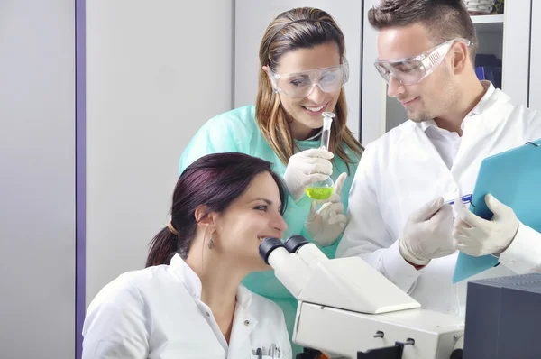 Jovens cientistas que estudam novas substâncias ou vírus em microscópio — Fotografia de Stock