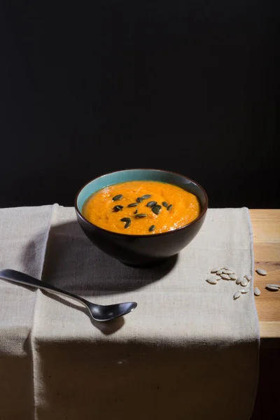 An orange pumpkin soup in a bowl on a linen cloth with pumpkin seeds and a spoon — Stock Image Orange Pumpkin Soup Bowl Linen Cloth Pumpkin Seeds Spoon Stock Photo