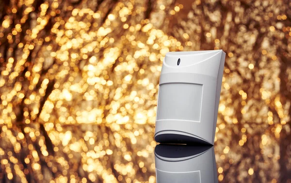 White plastic alarm motion sensor with fancy shiny gold background full of sparks out of focus. — Stock Photo, Image