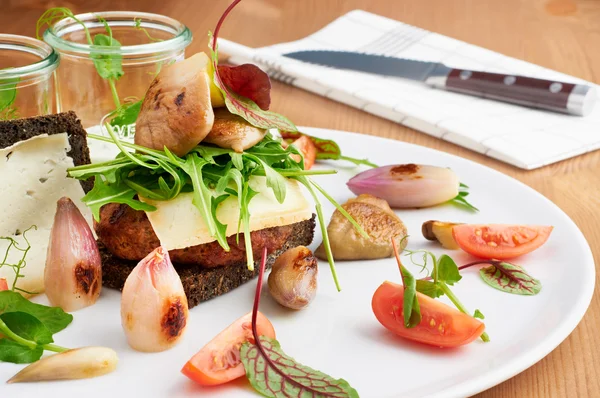 Deliciosa hamburguesa servida en plato blanco con cebolla, tomate, rúcula y pan de centeno. Cuchillo de fondo para cortar la comida . — Foto de Stock